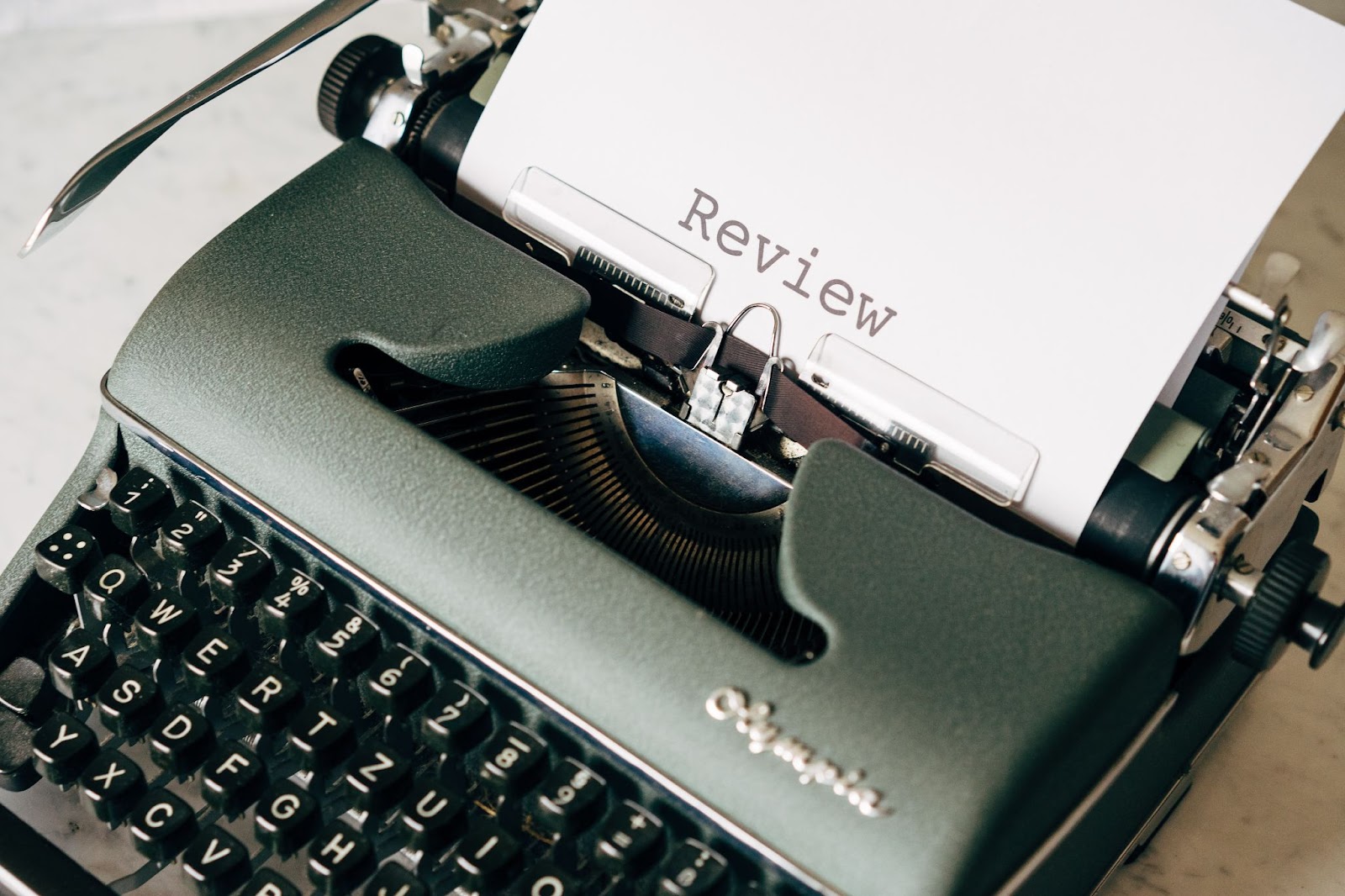 Eine schwarze Schreibmaschine, aus der ein beschriebenes Blatt Papier mit der Aufschrift “REVIEW” steht - Payone vs SumUp. Wer gewinnt den Bewertungsvergleich?